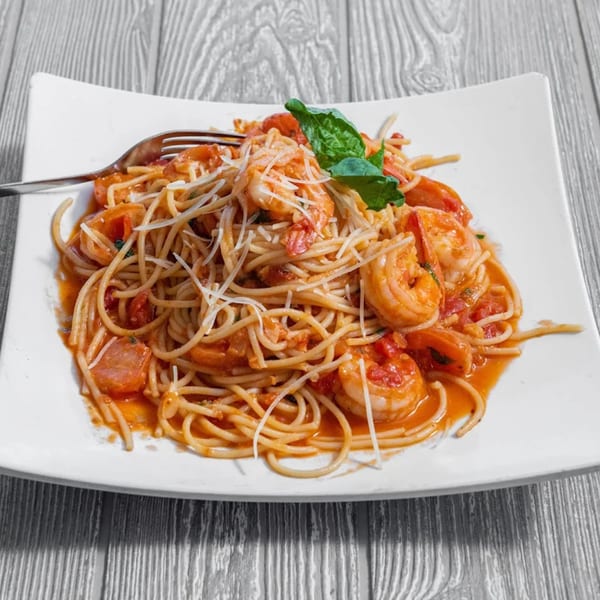 Shrimp scampi pasta with cherry tomatoes, basil, and parmesan cheese on a white plate.