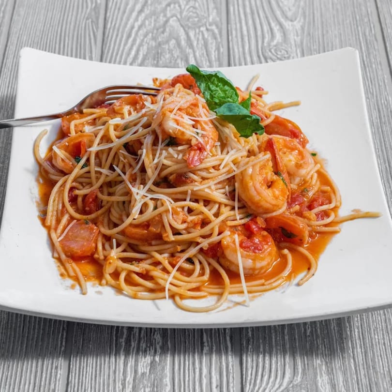Shrimp scampi pasta with cherry tomatoes, basil, and parmesan cheese on a white plate.