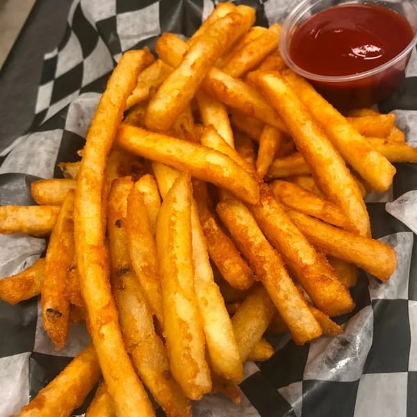 A basket of golden french fries with a side of ketchup, served on checkered paper.