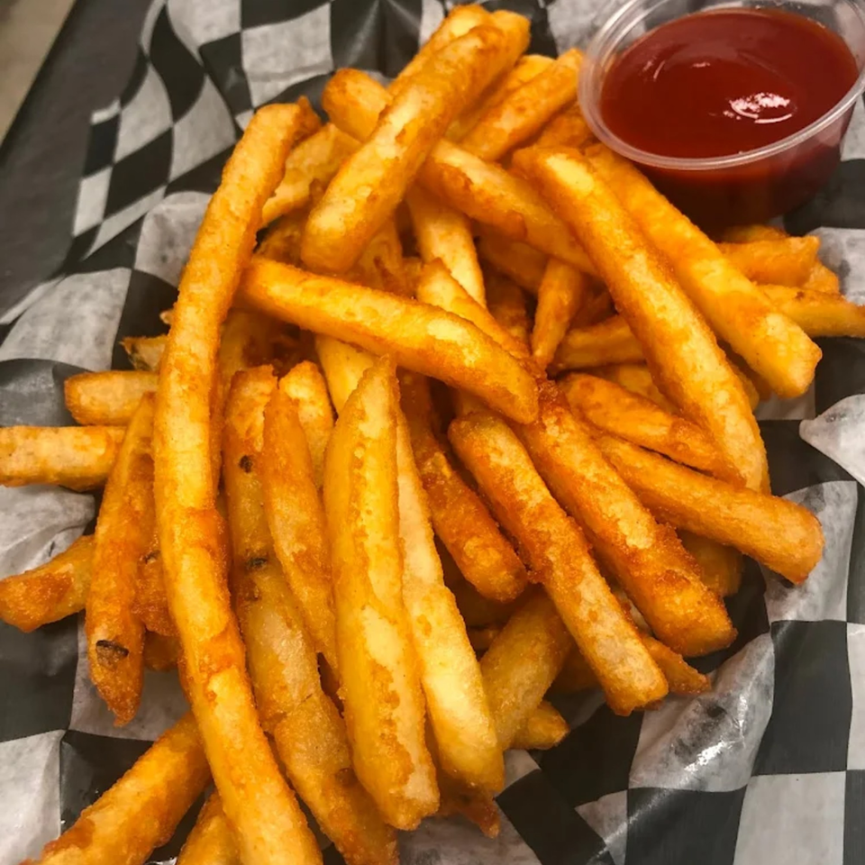 A basket of golden french fries with a side of ketchup, served on checkered paper.
