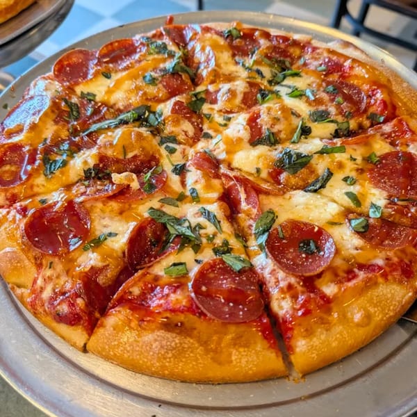 A freshly baked pepperoni pizza, topped with melted cheese and basil, on a metal serving tray.