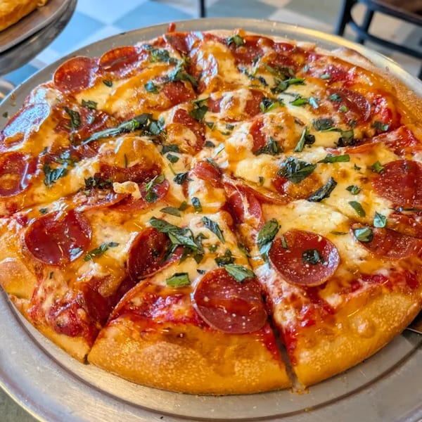 A freshly baked pepperoni pizza, topped with melted cheese, tomato sauce, and basil, on a metal tray.